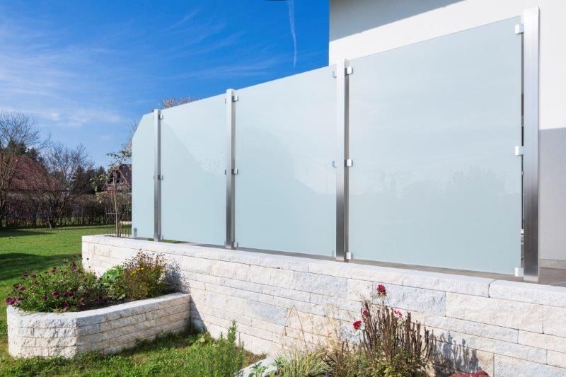 Ein transparenter Glaszaun und ein weißer Zaun umrahmen einen schönen Garten, der zum Entspannen einlädt.